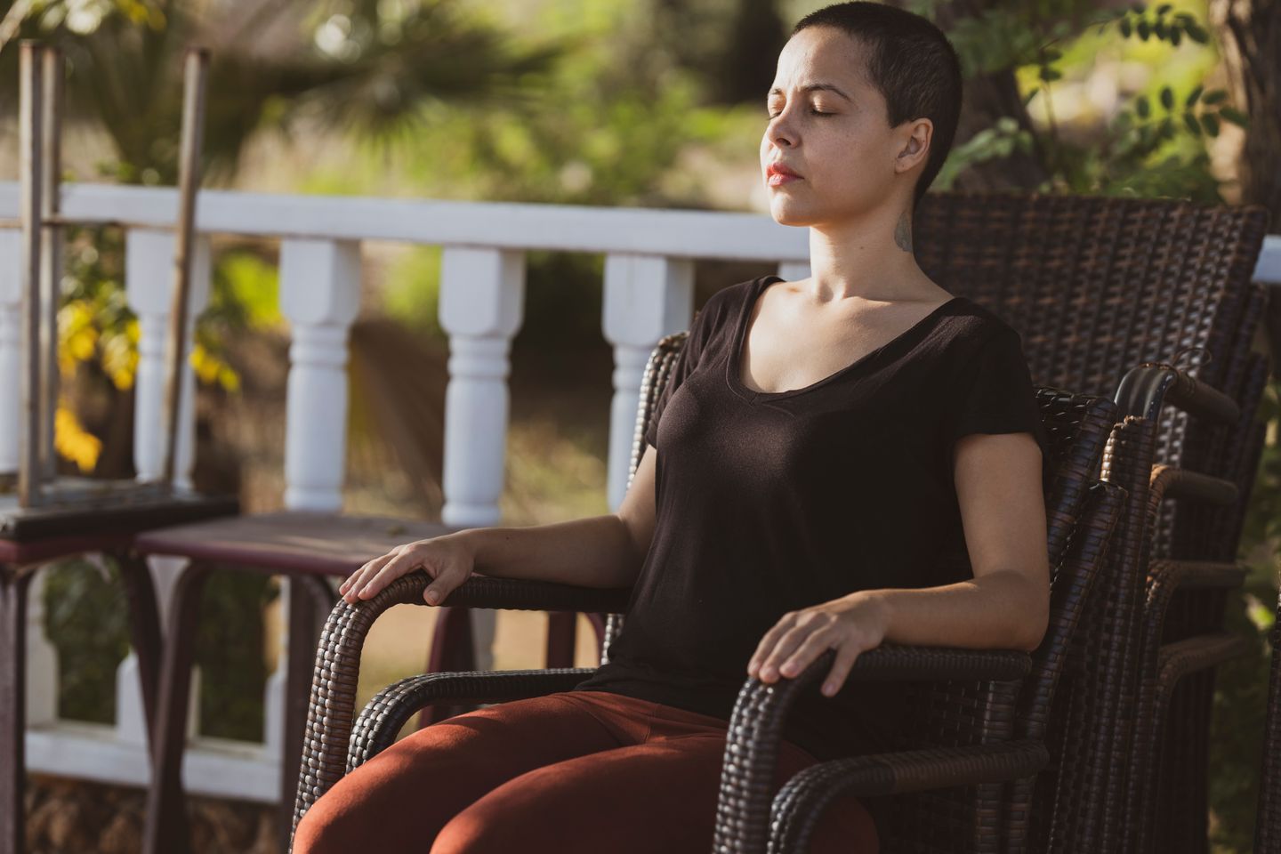 A woman in meditation with eyes closed sitting on a chair outdoors in the sunlight.