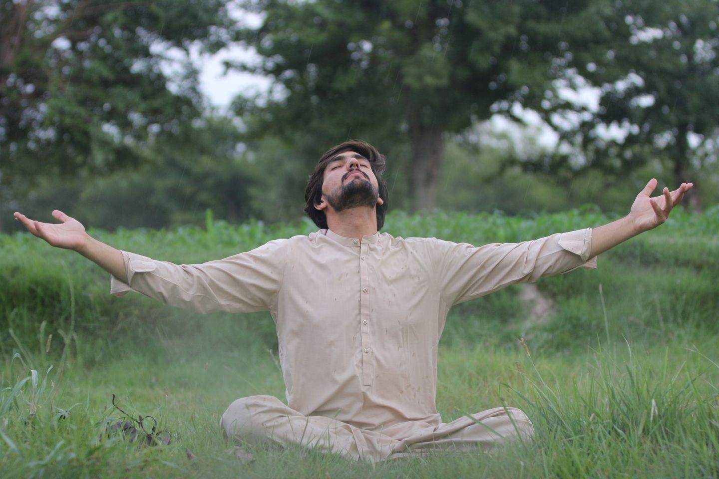 A man meditates serenely in a lush green landscape, embracing nature's tranquility.
