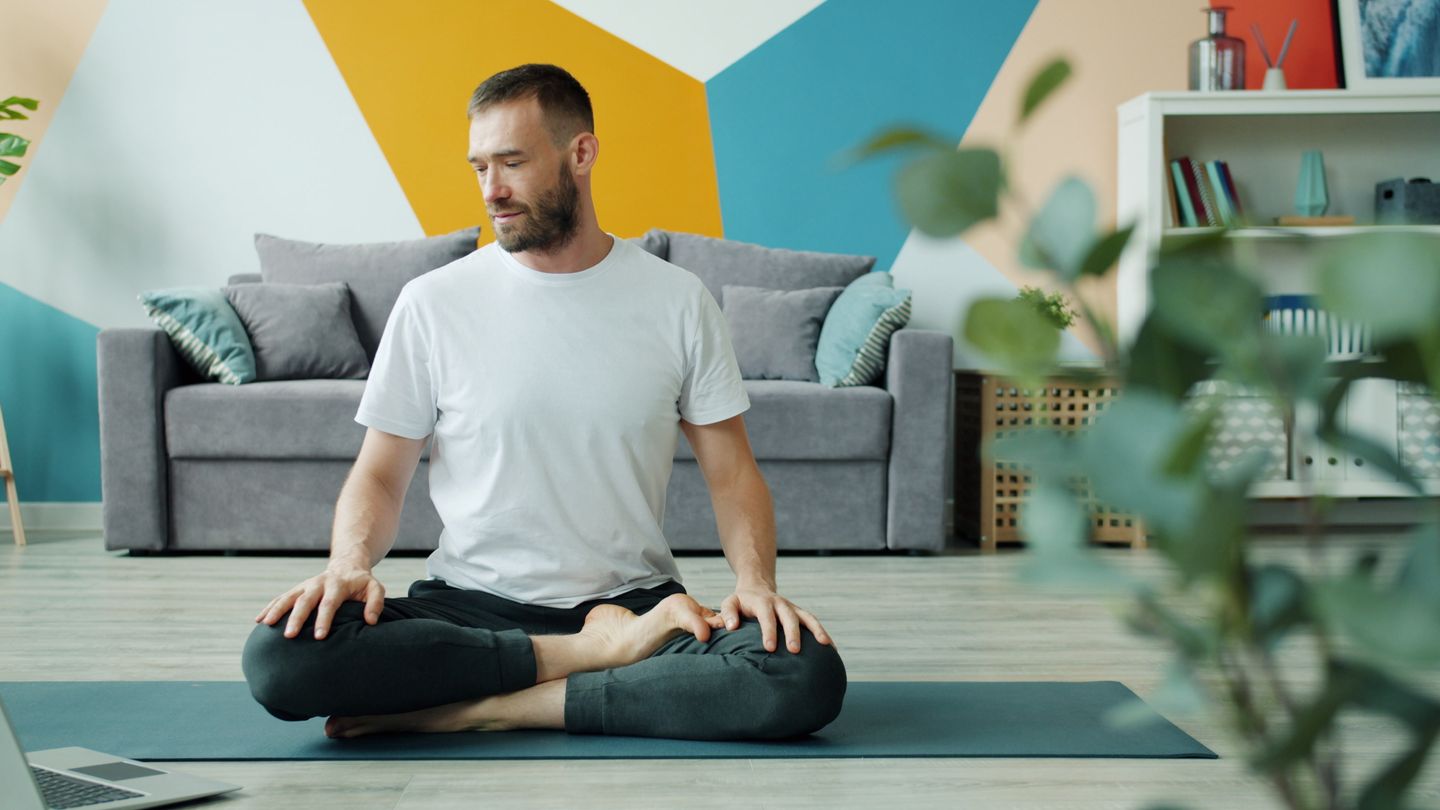 A man sitting in a yoga pose on a mat indoors, relaxed and mindful.